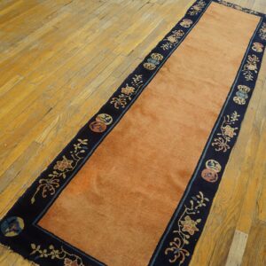 A runner rug with a solid salmon field and a dark blue floral border rests on distressed wood flooring.