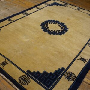 Golden beige rug with a navy blue border and key patterns sits on rustic wood planks.