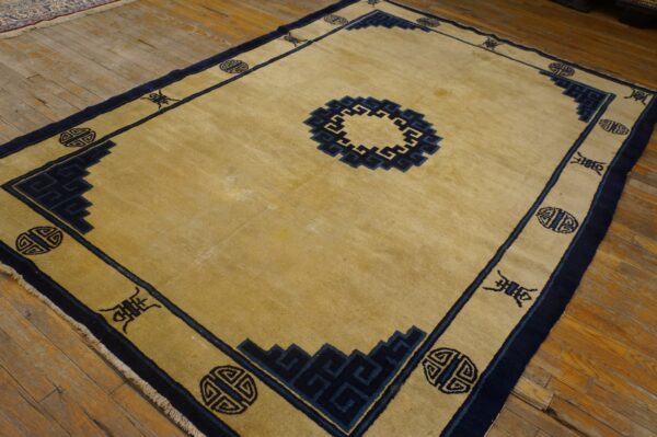 Golden beige rug with a navy blue border and key patterns sits on rustic wood planks.