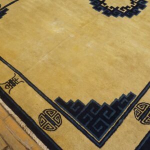 Golden yellow rug with a navy blue geometric border and central design on distressed wood flooring.