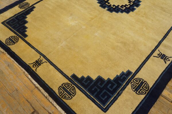 Golden yellow rug with a navy blue geometric border and central design on distressed wood flooring.