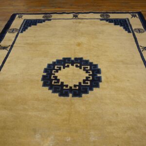 Pale gold rug with dark blue geometric border and center medallion on wooden flooring.