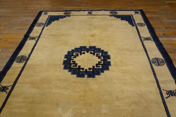 Pale gold rug with dark blue geometric border and center medallion on wooden flooring.