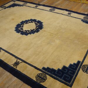 Tan rug featuring a geometric navy blue border and central medallion rests on plank wood flooring.