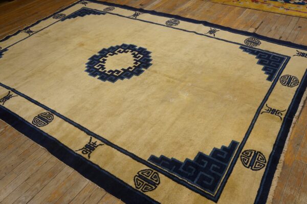 Tan rug featuring a geometric navy blue border and central medallion rests on plank wood flooring.