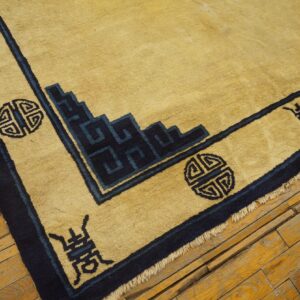 Gold rug corner with navy border showing geometric key patterns and symbols on rough wooden flooring.
