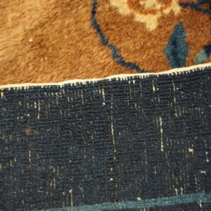 Detailed view of a high pile brown rug with blue floral patterns transitioning to a tightly woven navy border.
