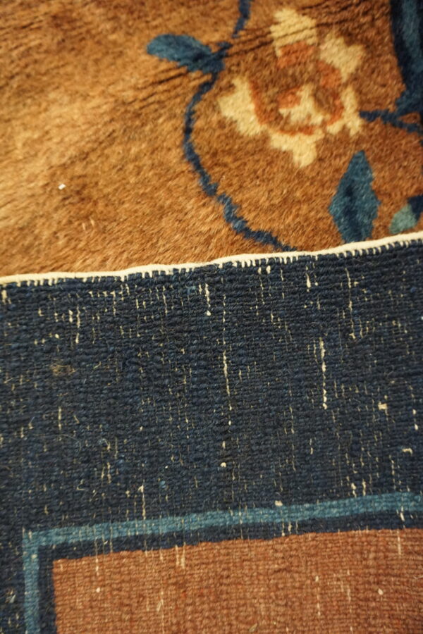 Detailed view of a high pile brown rug with blue floral patterns transitioning to a tightly woven navy border.