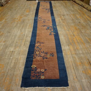 A reddish-brown floral runner rug with a navy border sits on a worn wood plank floor.