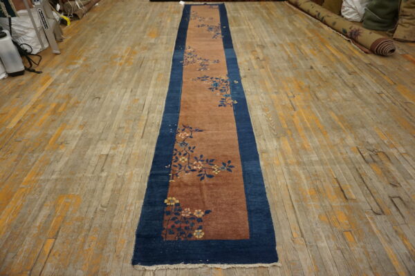 A reddish-brown floral runner rug with a navy border sits on a worn wood plank floor.