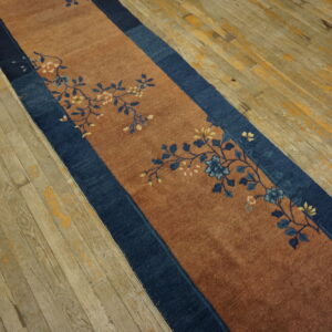 Rust runner rug with a navy border and blue floral pattern rests on gray and yellow distressed wood flooring.