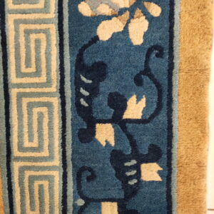 Blue rug detail showing a beige floral pattern, dark scrolling lines, and a light tan meander border.