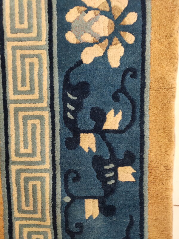 Blue rug detail showing a beige floral pattern, dark scrolling lines, and a light tan meander border.