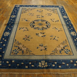 Gold field rug featuring scattered pink and blue florals and a wide blue patterned border on wood floors.