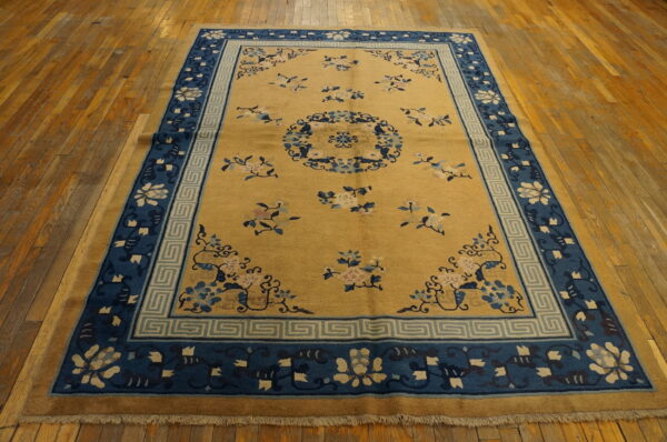 Gold field rug featuring scattered pink and blue florals and a wide blue patterned border on wood floors.