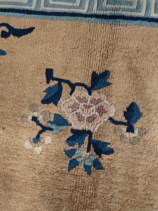 Tan rug detail features a pink floral motif, blue leaves, and a geometric blue border.