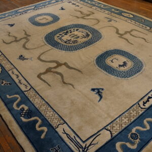 Large beige rug featuring blue scale motifs and abstract symbols within a detailed blue border on wood floors.