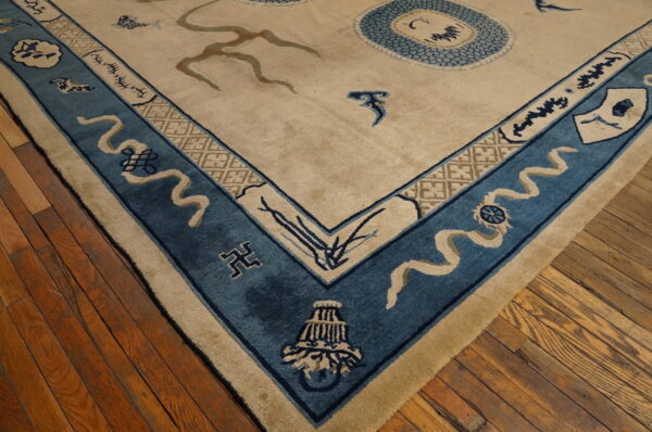 Plush beige rug corner features a wide blue border with symbolic tan ribbon motifs on distressed wood floors.