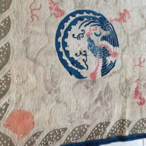 Beige carved rug featuring a central blue bird, pink accents, and a geometric dotted border pattern.