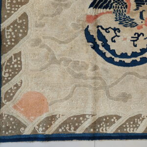 Close-up of a carved beige rug featuring a navy blue circular motif, coral accents, and taupe wave border.