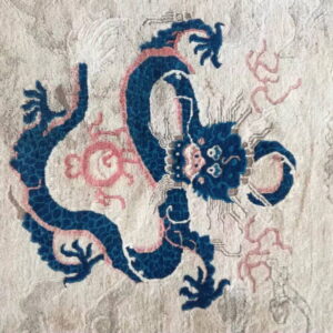 Textured rug detail with a blue dragon design accented by pink on a beige textured background.