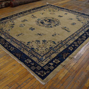 Tan rug with indigo blue floral borders and a central medallion lying on glossy wood plank flooring.
