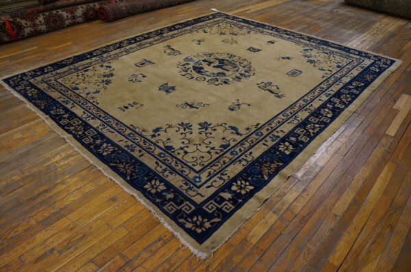 Tan rug with indigo blue floral borders and a central medallion lying on glossy wood plank flooring.