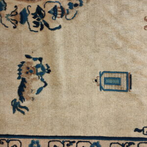 Detailed view of a light tan rug featuring stylized deep blue and rust-colored traditional patterns.