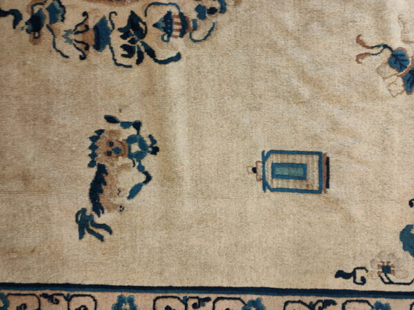 Detailed view of a light tan rug featuring stylized deep blue and rust-colored traditional patterns.
