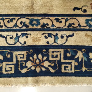 Tan rug border featuring navy blue, teal, and rust motifs, including scrolling vines and geometric fretwork.