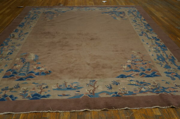 Rectangular taupe rug featuring a wide blue and dark brown scenic border on wood flooring.