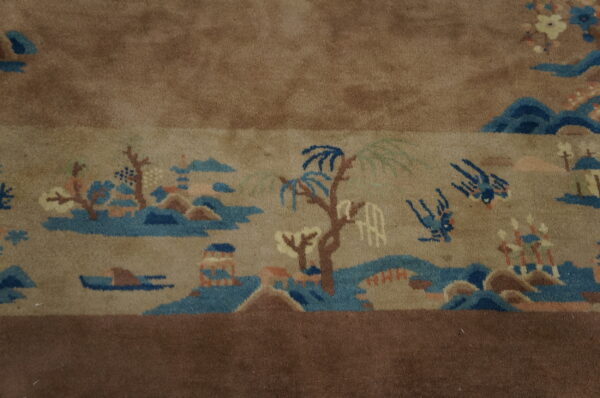 Detailed view of a tan rug with an elaborate scenic pattern bordered by solid medium brown pile.