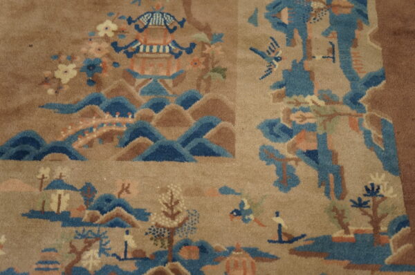 A plush tan rug features a detailed landscape design with blue mountains, a pagoda, trees, and flowers.