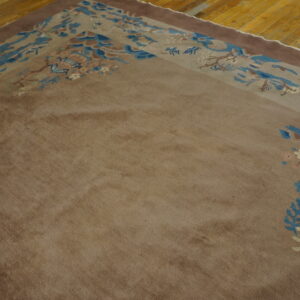 A brown rug with a detailed blue, cream, and tan landscape border sits on a golden wooden floor.