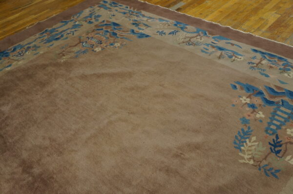 A brown rug with a detailed blue, cream, and tan landscape border sits on a golden wooden floor.