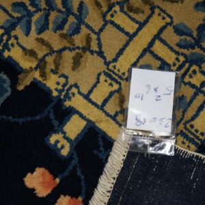 Close-up detail of a navy rug featuring a gold geometric lattice, blue leaves, peach flowers, and a white hang tag.