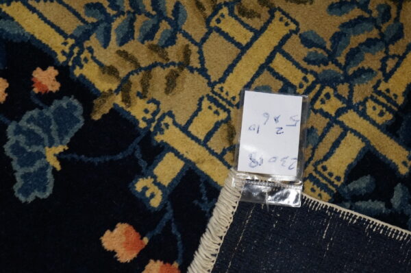 Close-up detail of a navy rug featuring a gold geometric lattice, blue leaves, peach flowers, and a white hang tag.