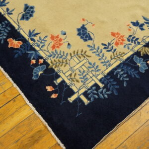 Beige rug corner featuring a navy border with blue, coral, and bamboo floral patterns on wood floors.