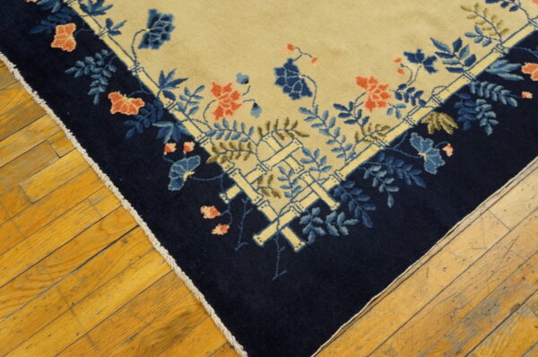 Beige rug corner featuring a navy border with blue, coral, and bamboo floral patterns on wood floors.