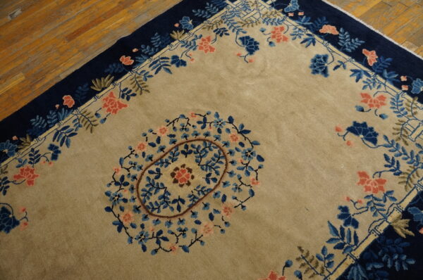Tan rug with a central floral medallion and a deep navy border over hardwood floors.