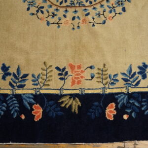 Detail of a beige rug with navy and coral floral designs above a dark blue border on wood flooring.