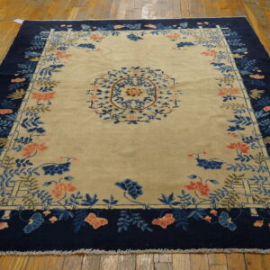 Beige rug with navy border features blue and coral floral motifs and a central medallion on wood floors.