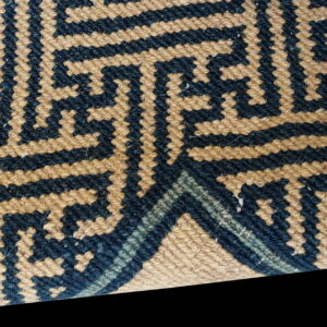 Woven rug detail featuring navy blue and tan interlocking geometric stepped key patterns.