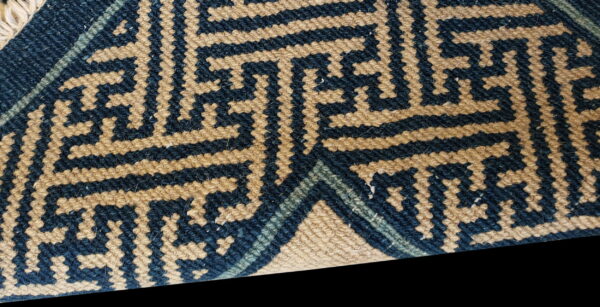 Woven rug detail featuring navy blue and tan interlocking geometric stepped key patterns.