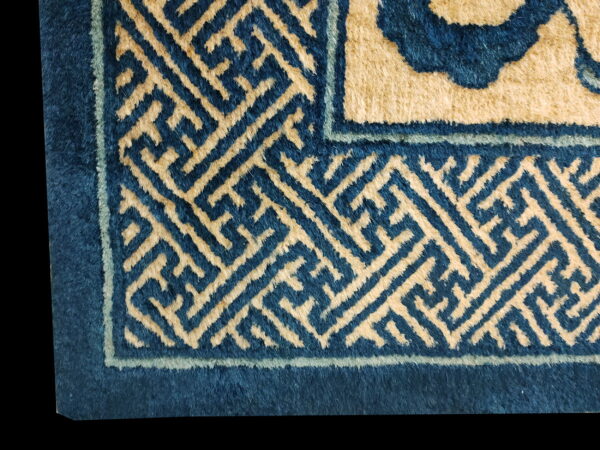 Detail of a high-pile rug featuring blue and beige geometric key pattern border designs.