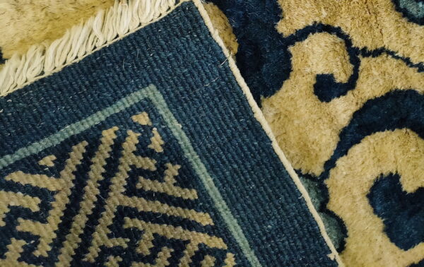 Close-up of a dark blue and tan high-pile rug showing the woven edge, geometric border, and fringe.