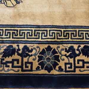 Plush tan rug featuring multiple navy blue borders with Greek key and stylized foliage designs.