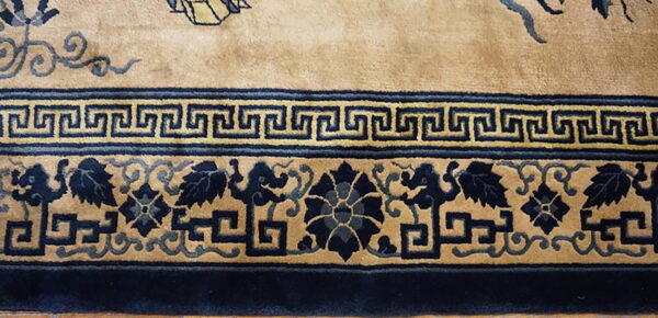 Plush tan rug featuring multiple navy blue borders with greek key and stylized foliage designs.