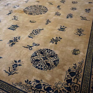 Angled view of a tan rug with scattered blue Oriental motifs and geometric banding along the border.