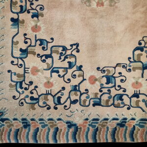 Pale pink low-pile rug corner featuring navy floral scrolls, coral blossoms, and a striped cloud border.